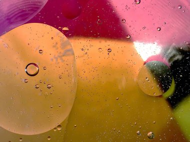 yüzen yağ damlaları farklı renklerde parıldıyor ve renkli bir arkaplanda hava kabarcıklarının yanında şekilleniyor.