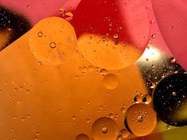 yüzen yağ damlaları farklı renklerde parıldıyor ve renkli bir arkaplanda hava kabarcıklarının yanında şekilleniyor.