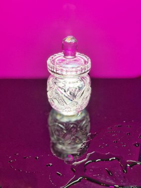 Aydınlatılmış kristal sürahi mor camda duruyor. Su damlalarının yansımasını görebilirsiniz.