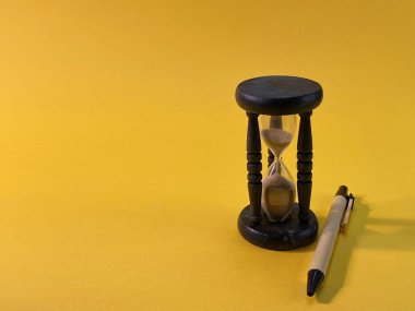 Sarı arka planda saati ölçen bir kum saati var, yanında da bir kalem.