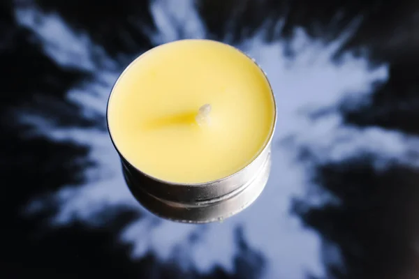 a yellow candle stands on a mirror that reflects a white BLOB on a black background.