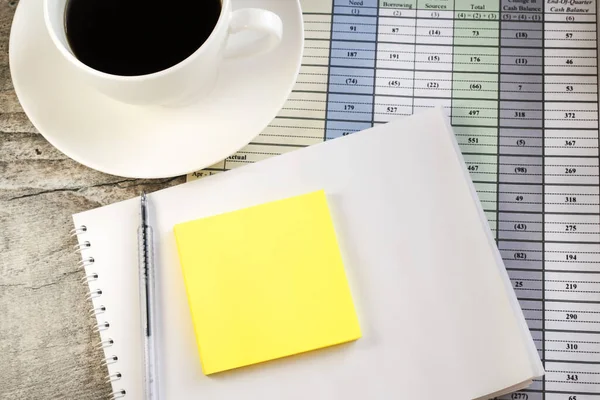 Documents with numbers have a Notepad on top of which is a blank sheet for notes. A Cup of coffee near the Notepad on the documents