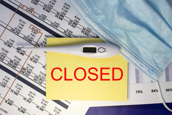 closed is written on a note sheet that lies with a thermometer and a medical mask on financial documents. The concept of quarantine and self-isolation during covid-19