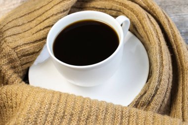 Sıcak bir kazağa sarılı beyaz bir kahve fincanı. Konfor ve sükunet kavramı