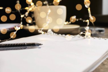 Not defteri ve kalem bulanık bir arkaplanda Bokeh ve beyaz bir kupa ile uzanır.