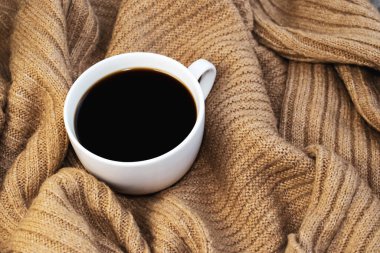 Sarı, sıcak bir kazağın üzerindeki beyaz kahve fincanının yakın çekimi. Konfor ve sükunet kavramı