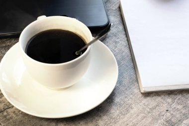 Not defteri ve dizüstü bilgisayarın yanındaki tahta masada beyaz bir fincan kahve duruyor. Çevrimiçi müzakere kavramı