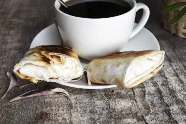 Ahşap masada ev yapımı kekler ve beyaz bir fincan kahve ile bir fincan çay tabağı var..