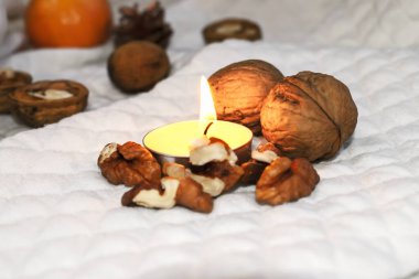 Cevizler arasında beyaz bir zeminde yanan sarı bir mum duruyor..