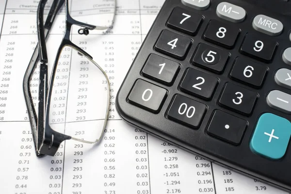 On financial documents with columns of numbers is a black calculator and glasses for vision. Business and financial concept