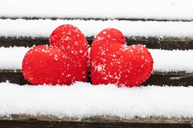 Karla kaplı tahta bir bankta duran iki kırmızı kalp..