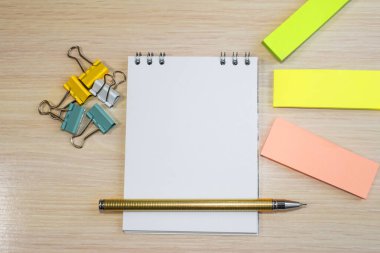 Açık tahta masanın üzerinde ataçlar ve renkli kağıtlar arasında bir kalem bulunan bir defter var. Mesaj için yer var. Konsept fotoğraf