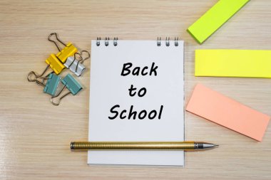 Okula dönüş, kağıt çıkartmaları ve kırtasiyelerin arasındaki ahşap bir masada duran bir deftere yazılmıştır. Konsept fotoğraf