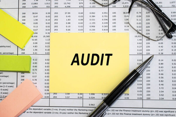 On the financial document near the eyeglasses and colored stickers there is a yellow sheet with the inscription audit. Business and financial concept