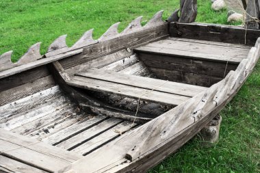 Kerestelerden yapılmış ahşap bir teknenin yakını yeşil çimlerle kaplı kıyıda duruyor.