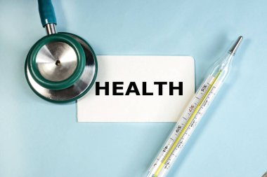 Stetoskop ve civa termometresi arasında mavi bir arkaplanda sağlık sözcüğünün yazılı olduğu beyaz bir sayfa vardır..