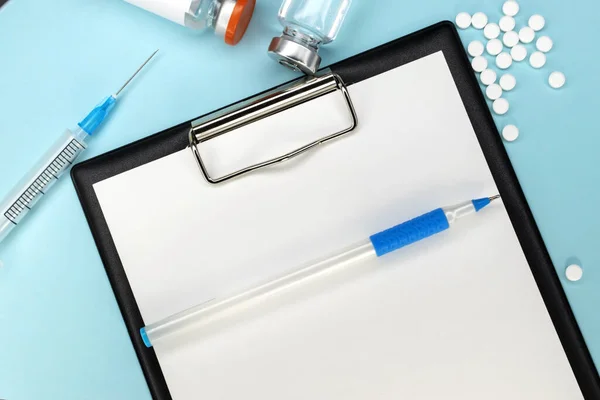 A stationery tablet with a pen lies on a blue background among medical preparations. Ampoule syringe and tablets. Medical concept.