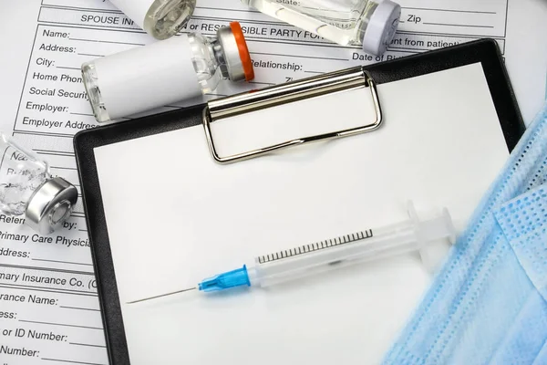 A face mask and a syringe lie on a stationery tablet that is located on the patient\'s medical questionnaire near the ampoule with the vaccine. Medical concept. Vaccination of the population