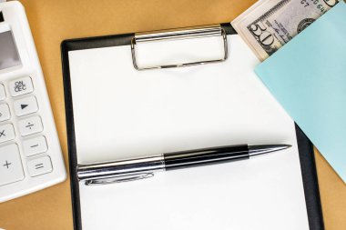 Beyaz boş bir çarşaf ve kalemle bir kırtasiye tableti. Beyaz hesap makinesi ve dolar. İş ve mali konsept.