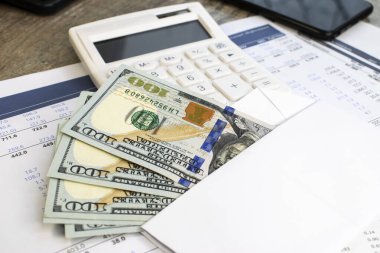 Beyaz bir zarfın içindeki dolarlar beyaz bir hesap makinesinin arka planına karşı bir iş belgesinde yatıyor. İş ve mali konsept