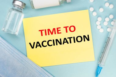 Tıbbi konsept. Üzerinde aşı için yazılan sarı bir yaprağın yakın çekimi var. Şırıngalı ve tıbbi maskeli bir ampul..