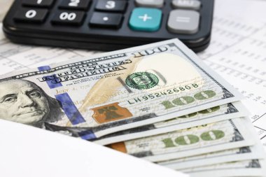 Siyah bir hesap makinesinin bulanık arka planında mali bir belgenin üzerinde duran dolarların yakın plan görüntüleri. İş ve mali konsept