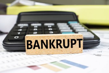 İflas kelimesi, siyah bir hesap makinesinin bulanık arka planında mali bir belgenin üzerinde duran tahta bir küpün üzerine yazılır. İş ve mali konsept