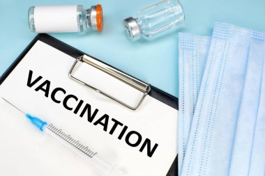 Aşı kelimesi bir kırtasiye tabletinde yazılı. Tıbbi yüz maskesi ve şırıngalı ampuller. Tıbbi konsept