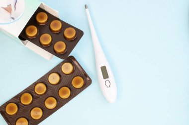 Elektronik beyaz termometre ve tabletler mavi arka planda ambalajla su toplamış. Metin için uzayı olan tıbbi bir kavram. Arkaplan