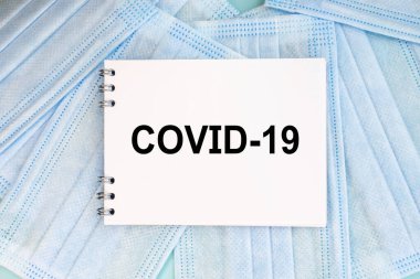 Tıbbi yüz maskelerinin üzerinde covid-19 yazılı bir defter var. Tıbbi konsept