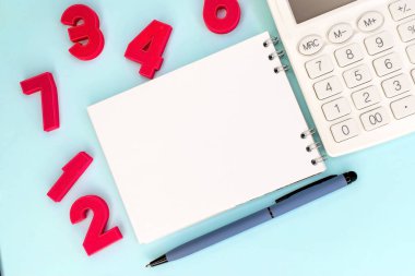 On a blue background next to red numbers and a white calculator with a blue pen there is a notebook with a blank white sheet. The concept of business and education. Template