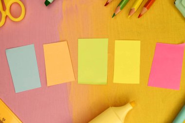 Kırtasiye malzemelerinin arasında boyanmış ahşap bir arka planda beş renkli kağıt parçası var. Şablon. Eğitim kavramı