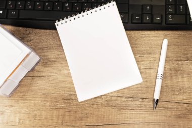 Beyaz bir kalemin yanında siyah bir klavyenin üzerinde boş beyaz bir sayfa bulunan bir defter. İnternette çalışıyorum. Şablon