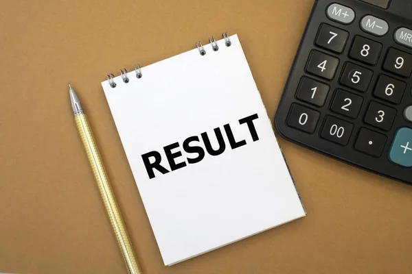 The word result is written on a notepad that lies next to a black calculator and a yellow pen. Business concept