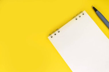 Sarı arka planda beyaz bir defter ve bir kalem var. Kavramsal fotoğraf. Arkaplan.