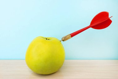 Ahşap yüzeyde içinde kırmızı dart olan yeşil bir elma var. Hedefler belirlemeyi ve onlara ulaşmayı kavra