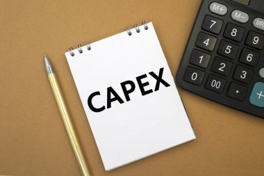 Capex kelimesi, siyah bir hesap makinesi ve sarı bir kalemin yanındaki kahverengi arkaplanda duran beyaz bir deftere yazılmıştır. İş ve mali konsept