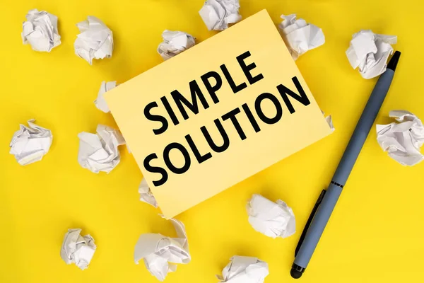 a simple solution is written on a yellow sheet that lies on crumpled white sheets of paper next to the pen.