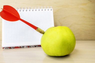 Ahşap bir yüzeyin arka planında, yeşil bir elmada kırmızı dart..