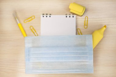 Ahşap masanın üzerinde kırtasiyenin yanında tıbbi yüz maskesi olan bir defter var. Eğitici kavram