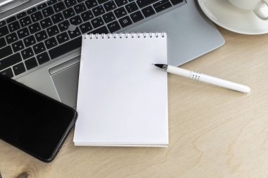 Ahşap bir masanın üzerinde gri bir dizüstü bilgisayar var. Üzerinde boş bir sayfa ve cep telefonu var. İnternetteki İş ve Eğitim