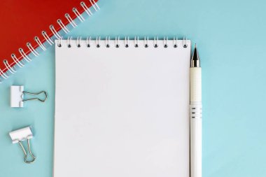 Üzerinde beyaz boş bir sayfa ve mavi arka planda bir kalem olan açık bir defter. Çalışma alanı