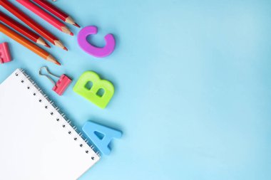 Okul eğitimi. Mavi arka planda not defteri olan harfler ve renkli kalemler. Boşluğu kopyala. Okula geri dönmek ya da tatile çıkmak.