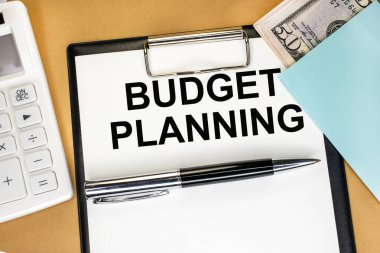 İş ve finansal konsept. Beyaz hesap makinesi ve dolarların arasında yer alan bir kırtasiye tabletindeki yazıt bütçe planlaması.
