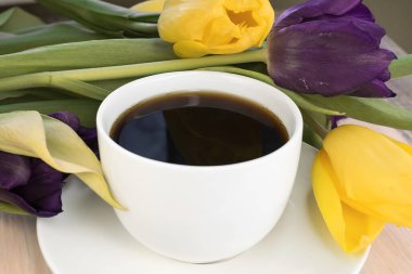 Bir buket lalenin arka planında beyaz bir fincan kahve. Duvar kağıdı ve tatil arkaplanı