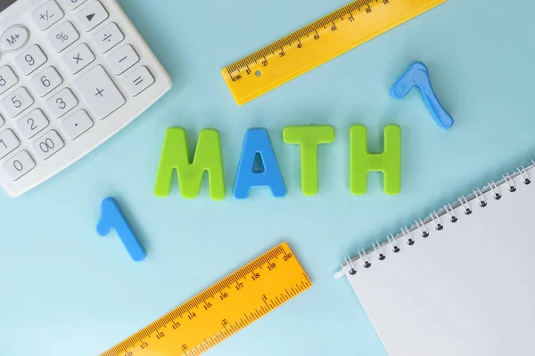 The word math is written in plastic letters. A white calculator with a notepad and two yellow rulers. Educational concept