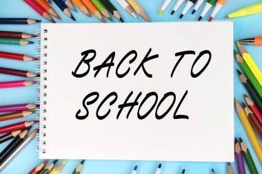 Okula dönüş renkli kalemler ve kalemler arasında mavi arka planda duran bir deftere yazılmıştır. Eğitici kavram