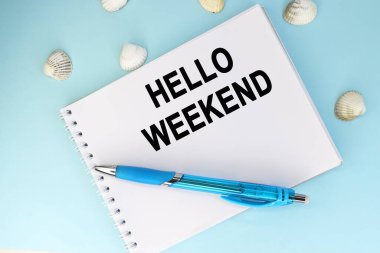 Hello Weekend, bir kalem ve deniz kabuğunun yanındaki mavi arka planda duran bir defterde yazılıdır..