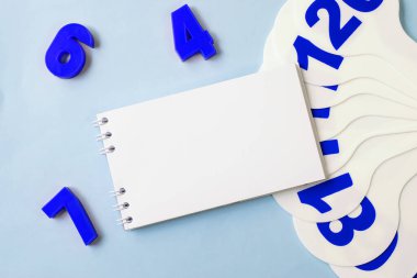 Mavi plastiğin yanındaki mavi arka planda beyaz boş bir sayfa ve üzerinde numaralar olan beyaz bir pervane. Eğitici kavram