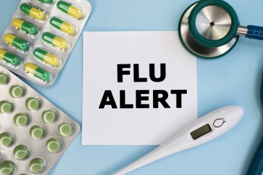 A white blank sheet on a blue background among the medicines. A stethoscope with a thermometer and pills in a blister. Medical concept